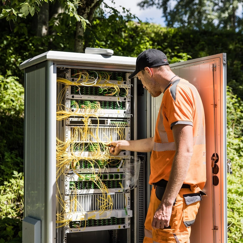 En mannlig ansatt jobber i et kabelskap for installering av fiber.